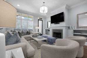 A modern living room with a sofa, armchairs, a coffee table, a fireplace, a television, and a chandelier.