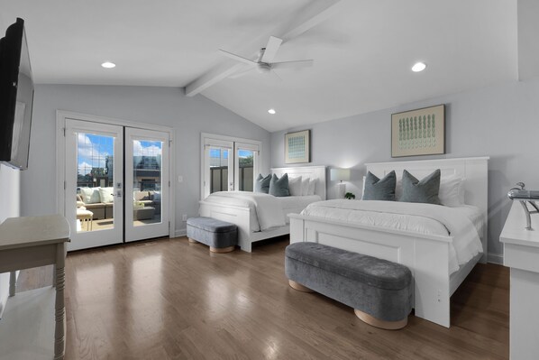 A modern bedroom with a large bed, a smaller bed, a ceiling fan, and a view through the glass doors.