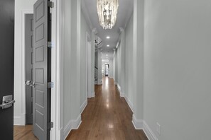 A hallway with a wooden floor, white walls, and a chandelier.