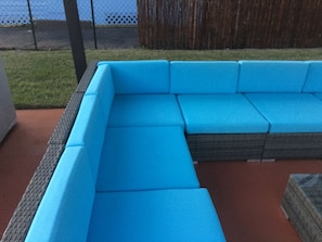 A blue sectional sofa with a woven seat and backrest, placed on a red outdoor floor. - Charming Bungalow House (West Palm Beach)