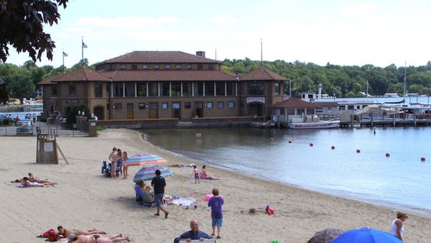 A beach with people sunbathing, umbrellas, and a building in the background. - Sleeps 15! DOWNTOWN LAKE GENEVA Fully Licensed for Weekend Rentals! (Lake Geneva)