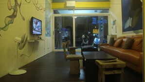 A room with a brown leather sofa, a wooden coffee table, a stone bench, a white fan, and a television on the wall.