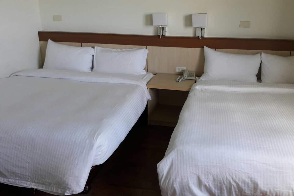 Una habitació d'hotel amb dos llits individuals, cadascun amb roba de llit blanca, un panell de fusta al capçal i làmpades de nit.