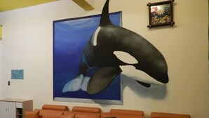 A room with a large whale mural on the wall, an orange sofa with cushions, and a small cabinet.