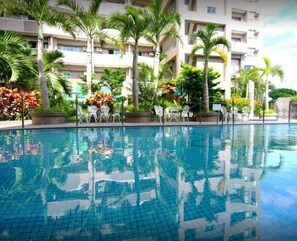 A swimming pool with clear water, surrounded by palm trees and a multi-story building with balconies. - Light Blue (Hengchun)