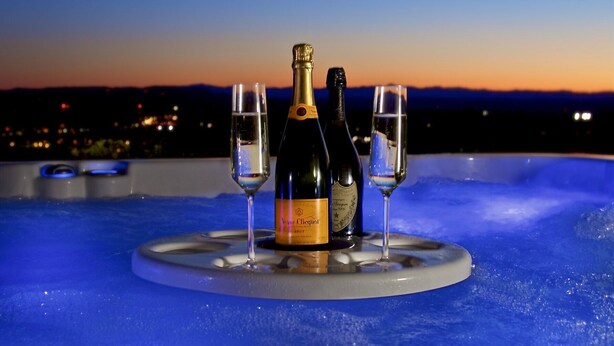 Et spabad med to glas og en flaske champagne, med en bysilhuet i skumringen i baggrunden.