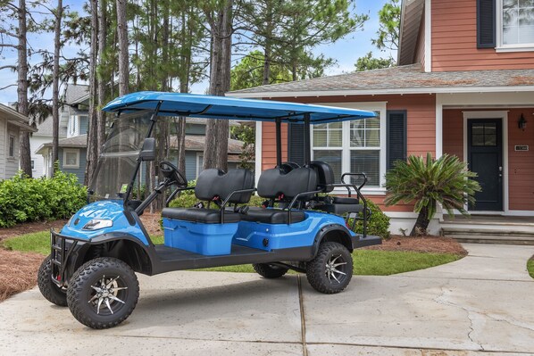 Un véhicule de golf bleu est garé devant une maison dotée d’un porche et d’un petit arbre.