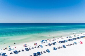 Une plage bordée de rangées de parasols et de chaises longues, une mer d’un bleu limpide et une rive de sable blanc.