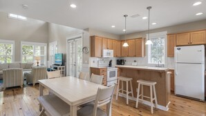A modern kitchen with wooden cabinets, a white refrigerator, and a dining area with a table and chairs. - Laurel Grove, Walk to Pool, 6-Seat Golf Cart (Miramar Beach)