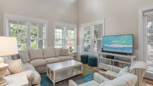 A living room with a beige sofa, striped armchairs, a coffee table, a TV, and a bookshelf. - Laurel Grove, Walk to Pool, 6-Seat Golf Cart (Miramar Beach)
