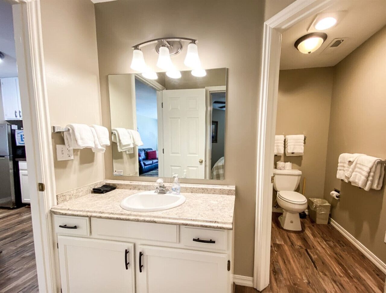 A bathroom with a white sink, a mirror, and a toilet. There are towels hanging on the wall.
