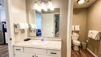 Une salle de bain avec un lavabo blanc, un miroir et des toilettes. Des serviettes sont accrochées au mur.