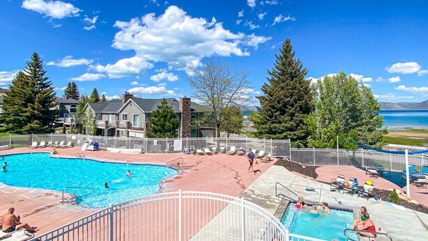 A swimming pool area with multiple pools, a white fence, and a view of mountains and a lake.