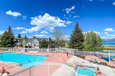 A swimming pool area with multiple pools, a white fence, and a view of mountains and a lake.