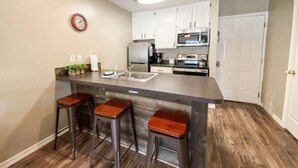 A kitchen with a central island, bar stools, white cabinets, a microwave, and a clock on the wall.