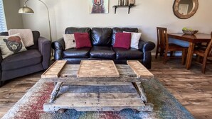 A living room with a black leather sofa, wooden coffee table, and a colorful rug.