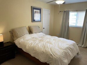 A bedroom with a bed, a nightstand, a framed picture on the wall, a door, and a window with curtains. - Near Sea World, BMT graduations, 7.5 Miles from the base, 25 Minutes to Airport (San Antonio)
