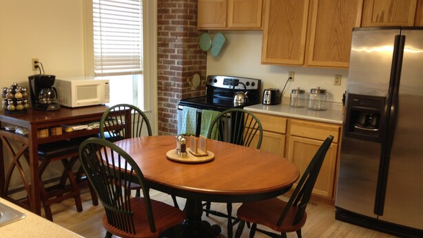 A kitchen with wooden cabinets, a stainless steel refrigerator, a microwave, a stove, and a dining table with chairs. - Keweenaw Vacation Rental - Great for families and groups- sleeps up to 7 (Ahmeek)