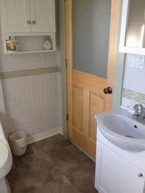 Une salle de bain avec un lavabo blanc, une porte en bois et un mur recouvert de carreaux.
