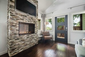Una sala de estar moderna con chimenea de piedra, un televisor de pantalla plana y vistas al exterior a través de una puerta.