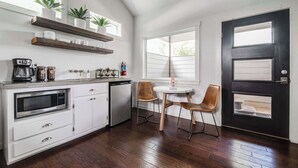 Une cuisine moderne avec des meubles blancs, un four à micro-ondes encastré et un coin café. On y trouve deux chaises et une petite table près d’une fenêtre.
