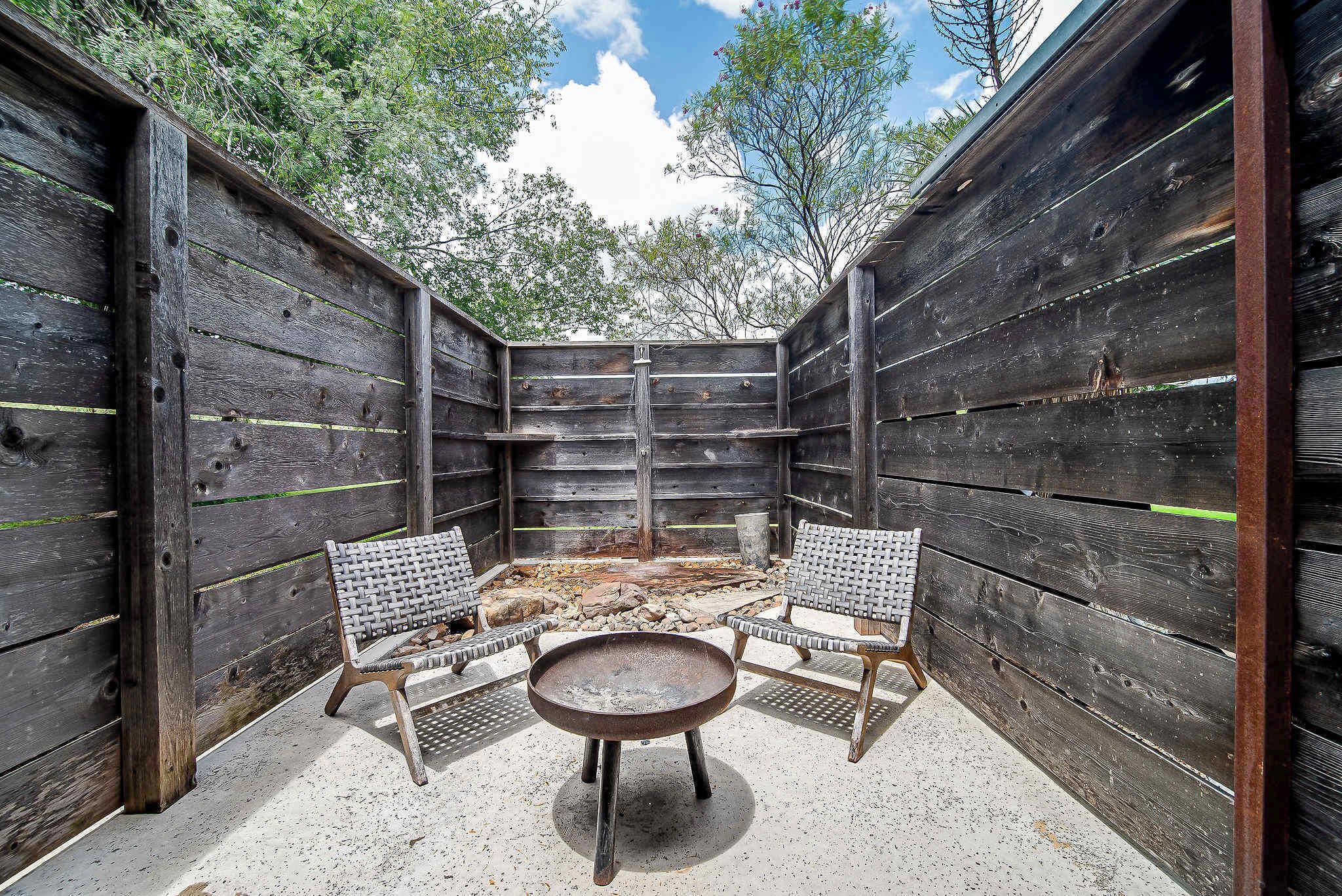 A wooden outdoor patio with two wicker chairs and a round table, surrounded by a rustic wooden fence.
