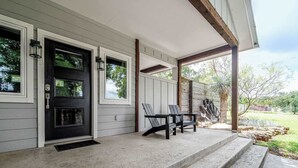 Une maison avec un porche couvert, une porte d’entrée noire et deux chaises.