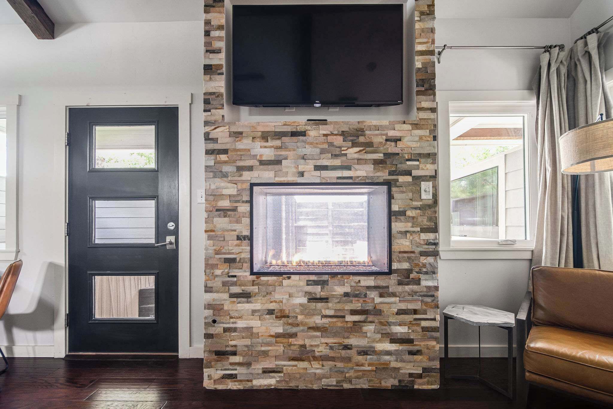 Una sala de estar con chimenea de piedra, televisor montado y ventana con cortinas.