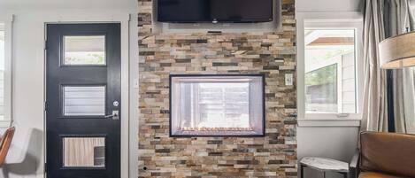 Una sala de estar con chimenea de piedra, televisor montado y ventana con cortinas.