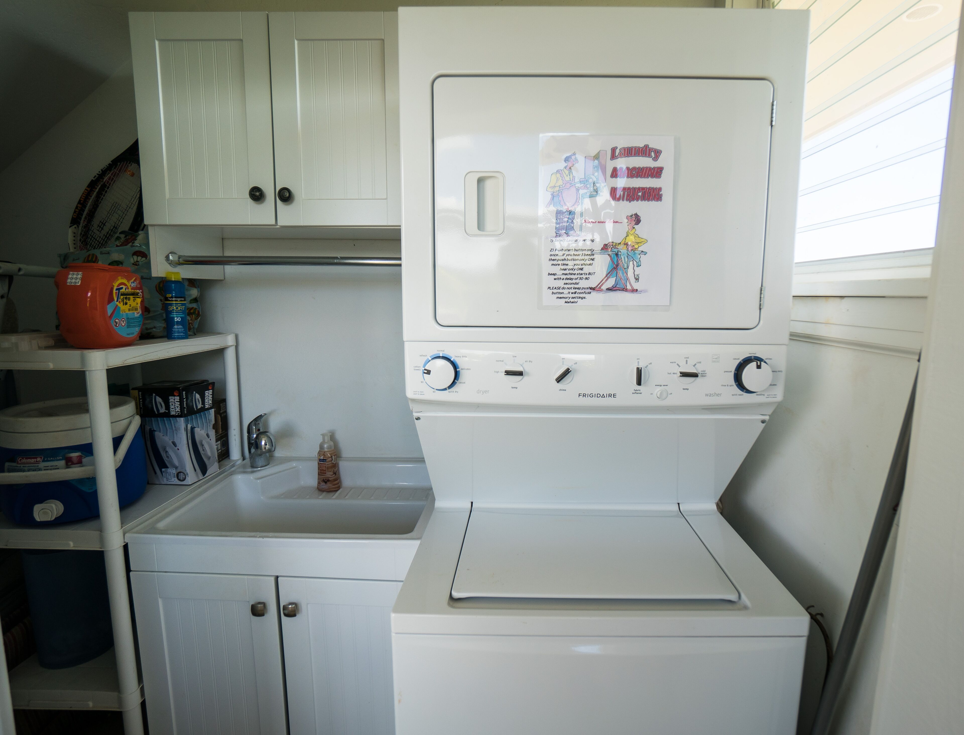 Une petite buanderie équipée d’un lave-linge et d’un sèche-linge blancs, d’un évier et d’une étagère contenant des produits de nettoyage.