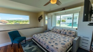 Ein Schlafzimmer mit Bett, Stuhl, Deckenventilator, Fenster und Fernseher.