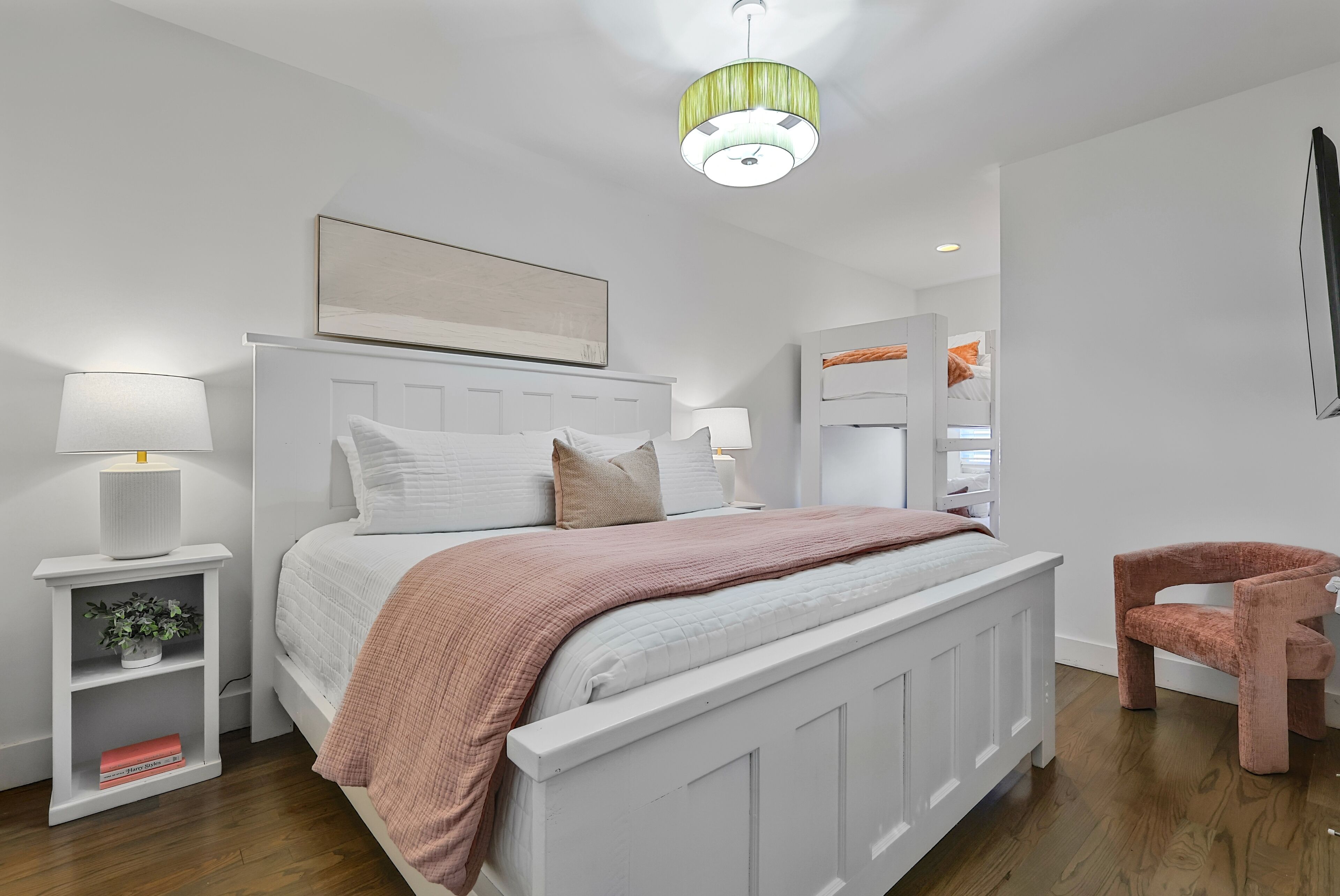 Une chambre à coucher comprenant un lit, des tables de chevet, une chaise, un luminaire suspendu et un tableau au mur.