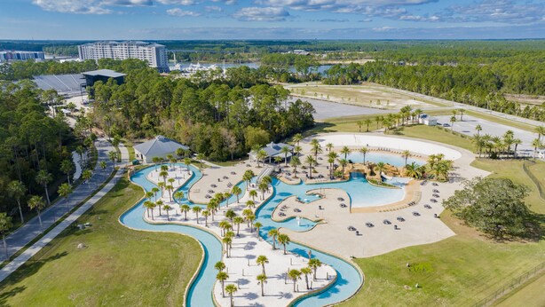 Vista aérea de un resort con varias piscinas, palmeras y un edificio grande al fondo.