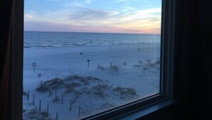 Uitzicht op een strand door een raam, met een heldere lucht en rustige zee.
