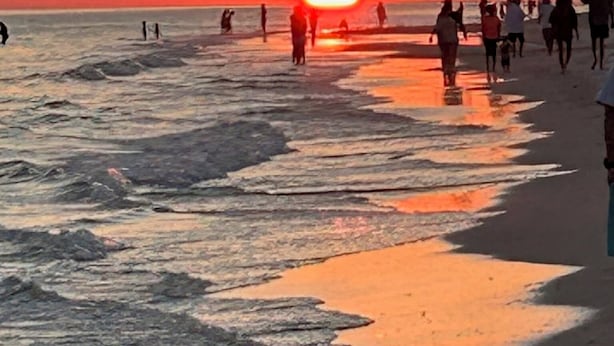Een strandscène met mensen die langs de kust wandelen tijdens de zonsondergang.