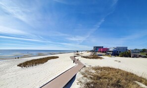A beach with a wooden boardwalk, a sandy path, and buildings in the background. - GULF COAST CONDO. ITS A GEM! (Biloxi)