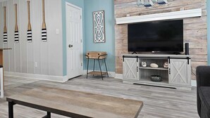 Een woonkamer met een televisie, een houten salontafel, een bankje en een wand met decoratieve objecten.