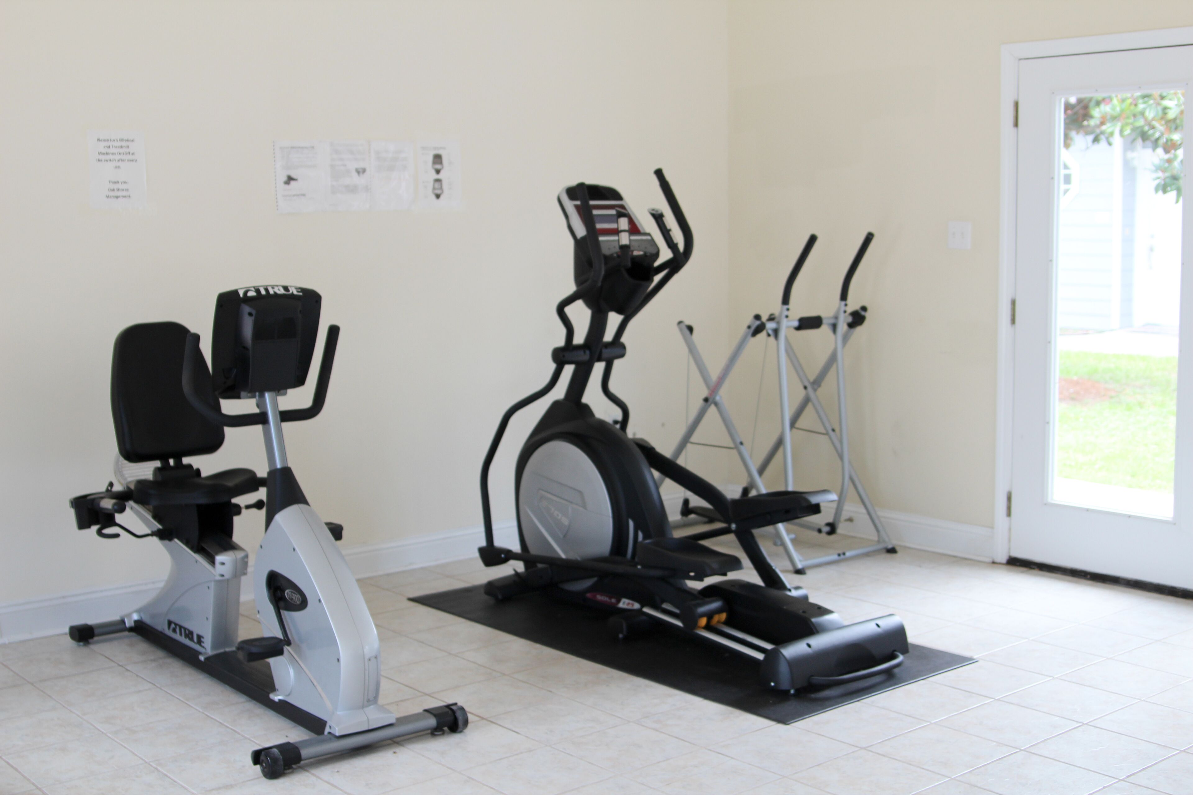Une salle de sport à domicile équipée d’un vélo elliptique, d’un vélo d’appartement et d’un tapis de course.