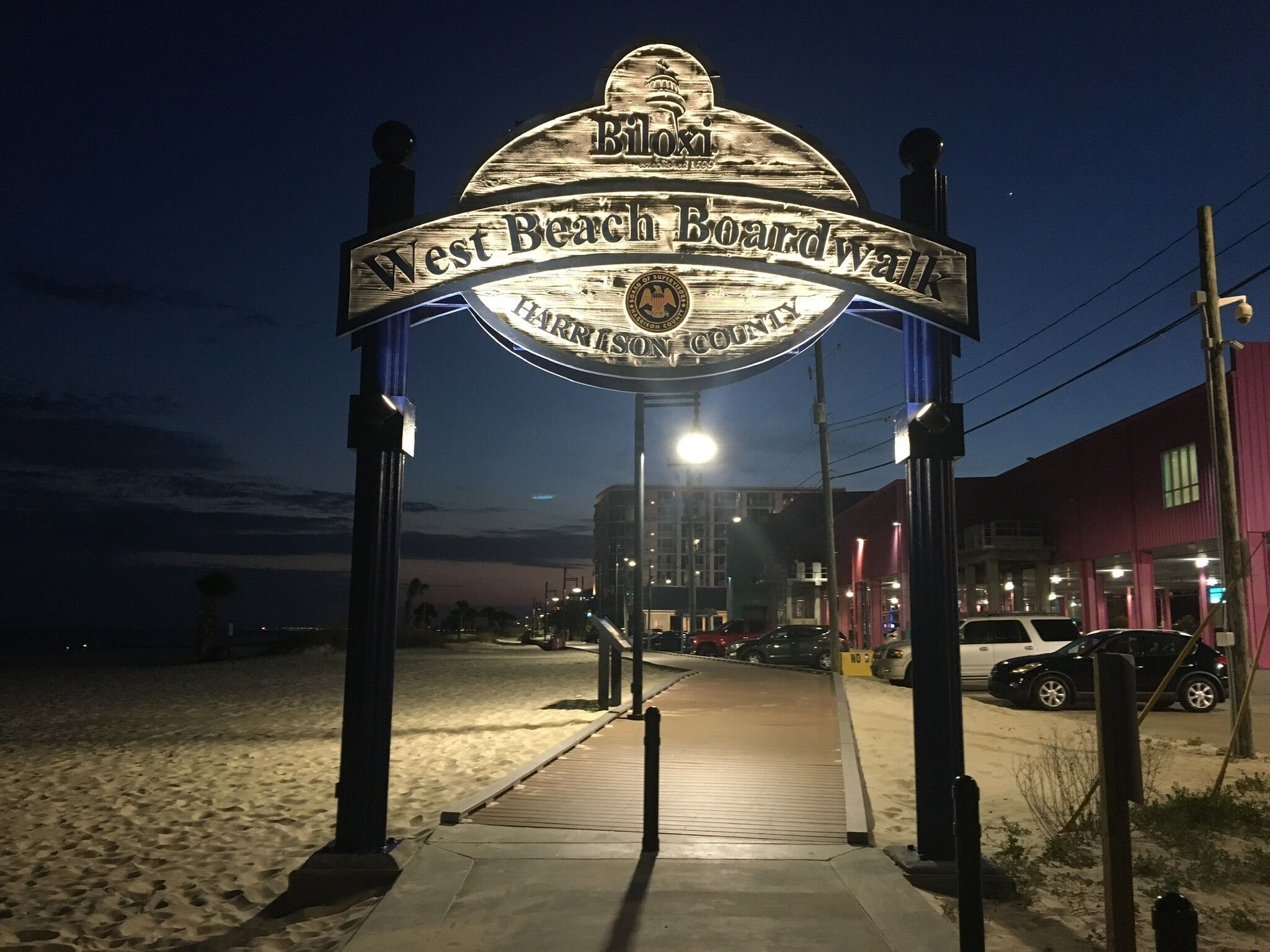 Eingang zu einem Strandpromenadenweg, mit einem Schild für die West Beach Promenadengegend, beleuchtet von Straßenlaternen.