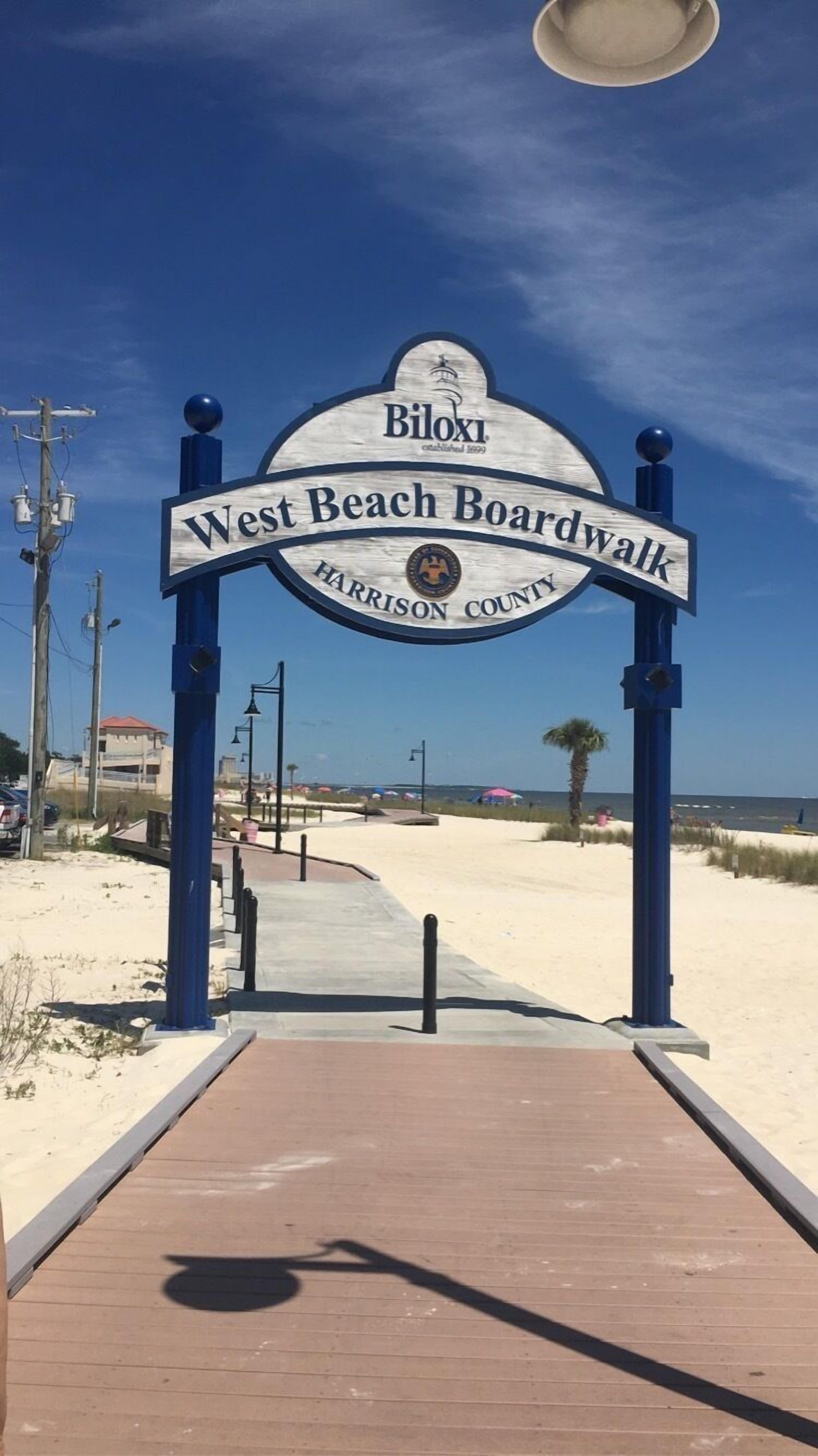 A wooden boardwalk sign with 'West Beach Boardwalk' and 'Harrison County' written on it.