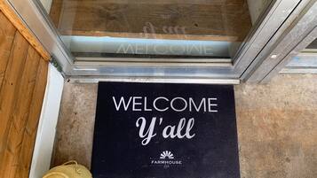 Eine Fußmatte mit der Aufschrift "WELCOME Y'all" und "FARMHOUSE loft", eine Glastür und ein gelbes Objekt auf dem Boden.