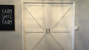 A white double door with a diagonal cross design, a blackboard with 'FARM sweet FARM' written on it, and a light switch on the wall. - The Farmhouse Loft "Greene County's Guesthouse" (Carrollton)