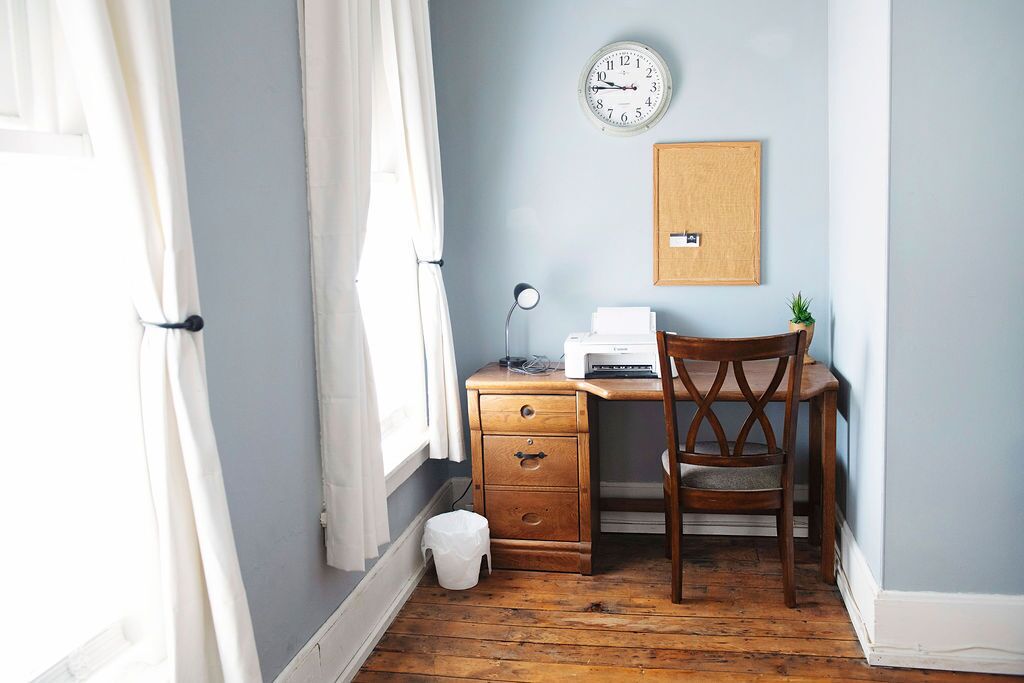 Una habitación pequeña con un escritorio de madera, una silla, un reloj y una planta.