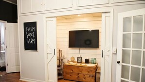 A room with a wooden chest, a mounted television, and a sign reading "FARM Sweet FARM". - The Farmhouse Loft "Greene County's Guesthouse" (Carrollton)