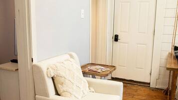 Un salon avec un fauteuil blanc, un plancher en bois, une porte blanche et une horloge murale.