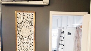 A room with a white armchair, a wooden side table, a decorative panel, and a view into a bathroom with a bathtub and shower curtain. - The Farmhouse Loft "Greene County's Guesthouse" (Carrollton)