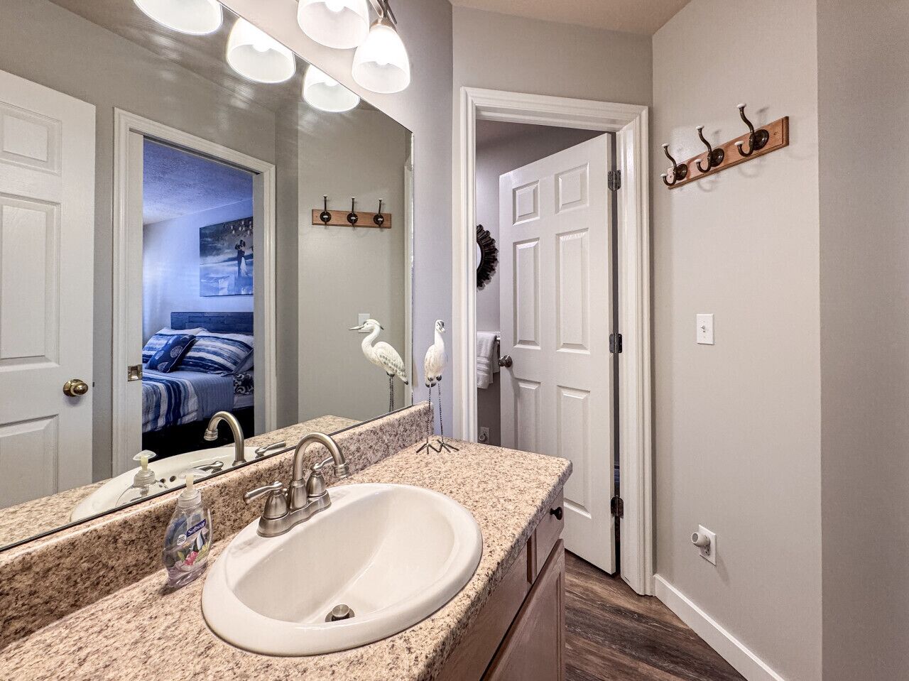 A bathroom with a granite countertop sink, a large mirror, and a wooden door with a towel rack.