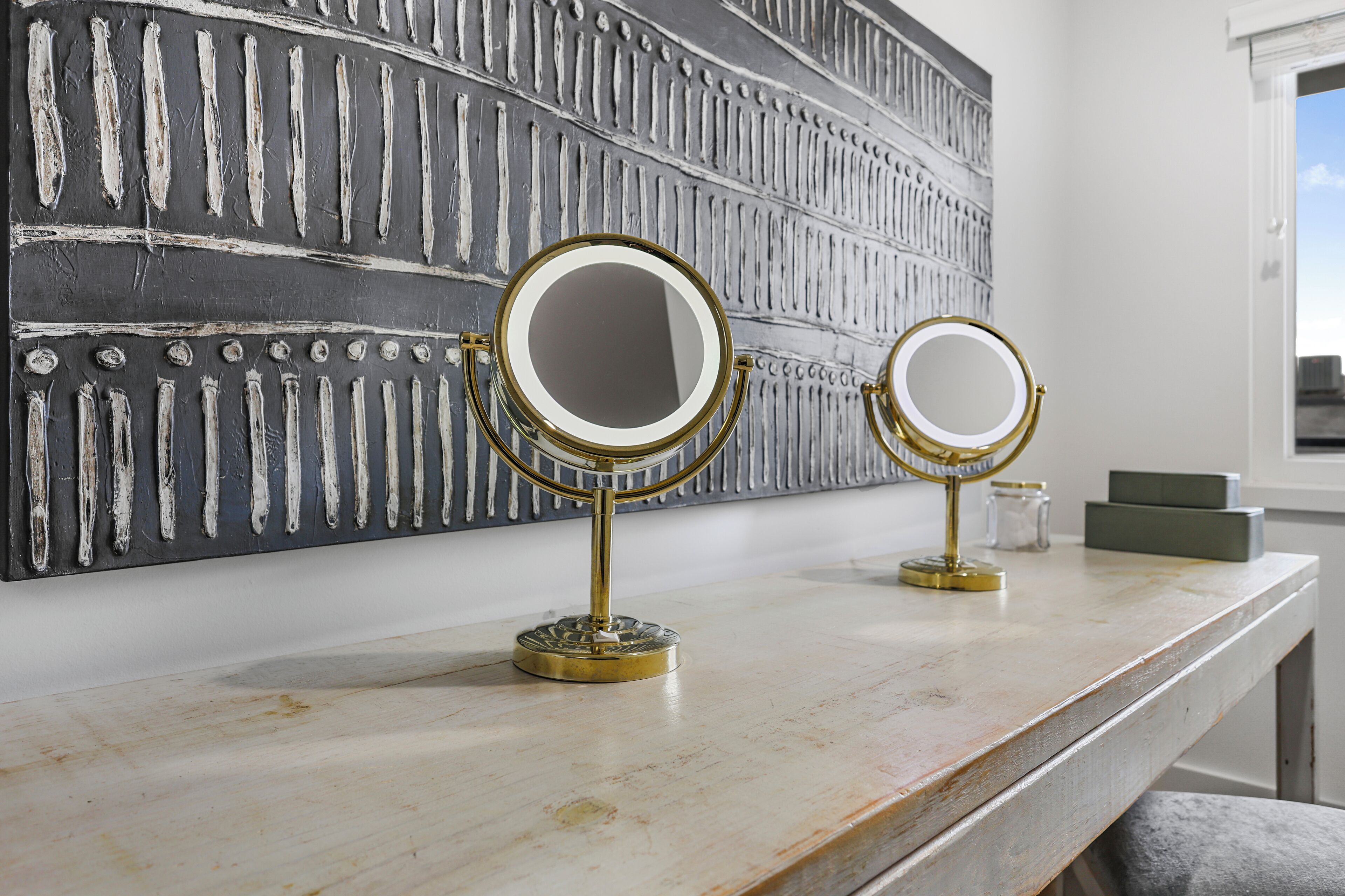 Two gold-framed mirrors on a white marble countertop with a decorative wall in the background.