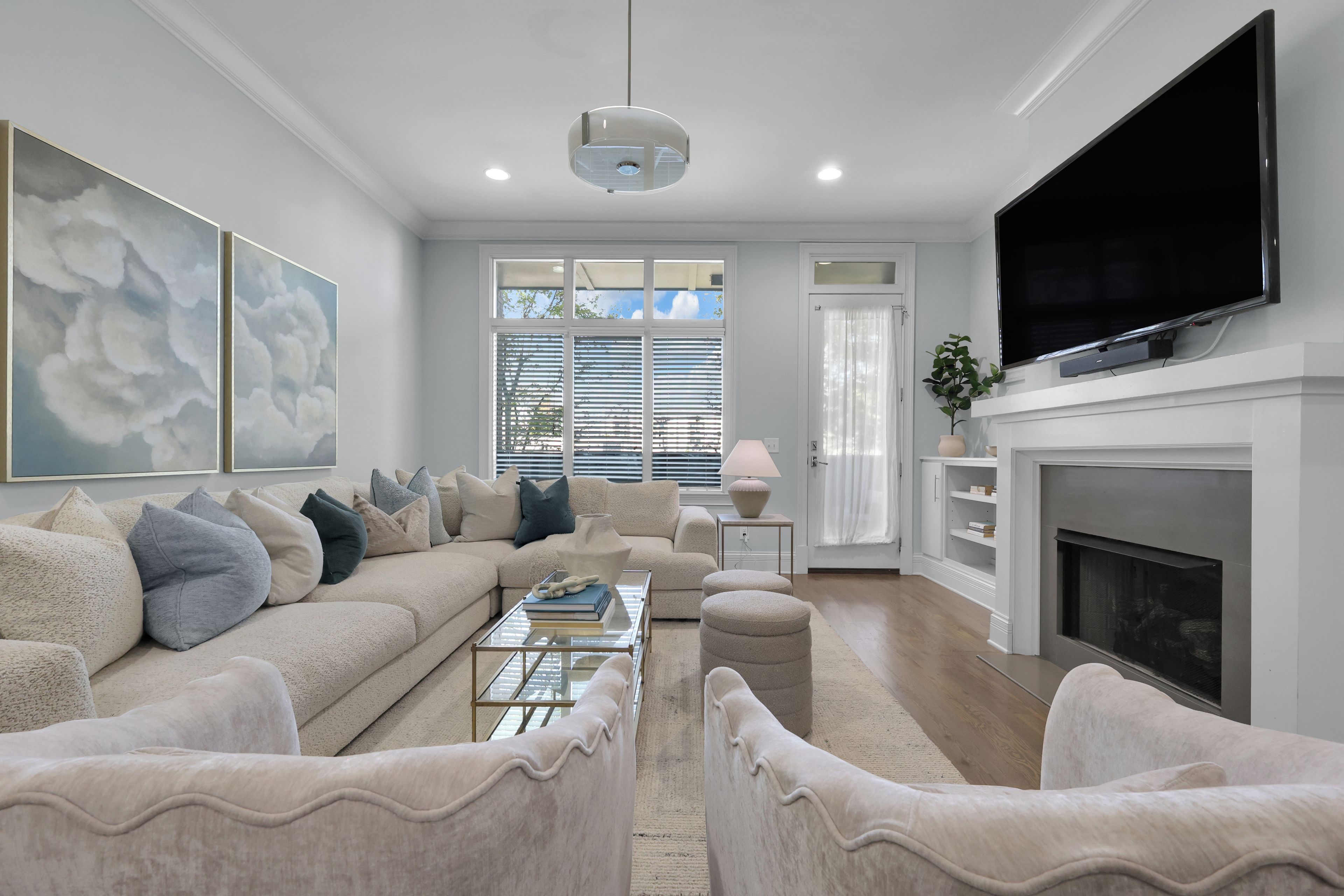 A modern living room with a sofa, ottomans, a coffee table, a flat-screen TV, and a fireplace.