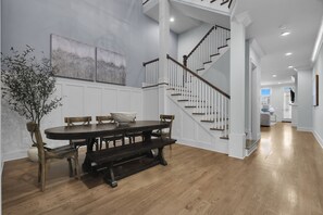 A dining area with a wooden table and benches, a staircase with white railings, and a hallway leading to a kitchen.